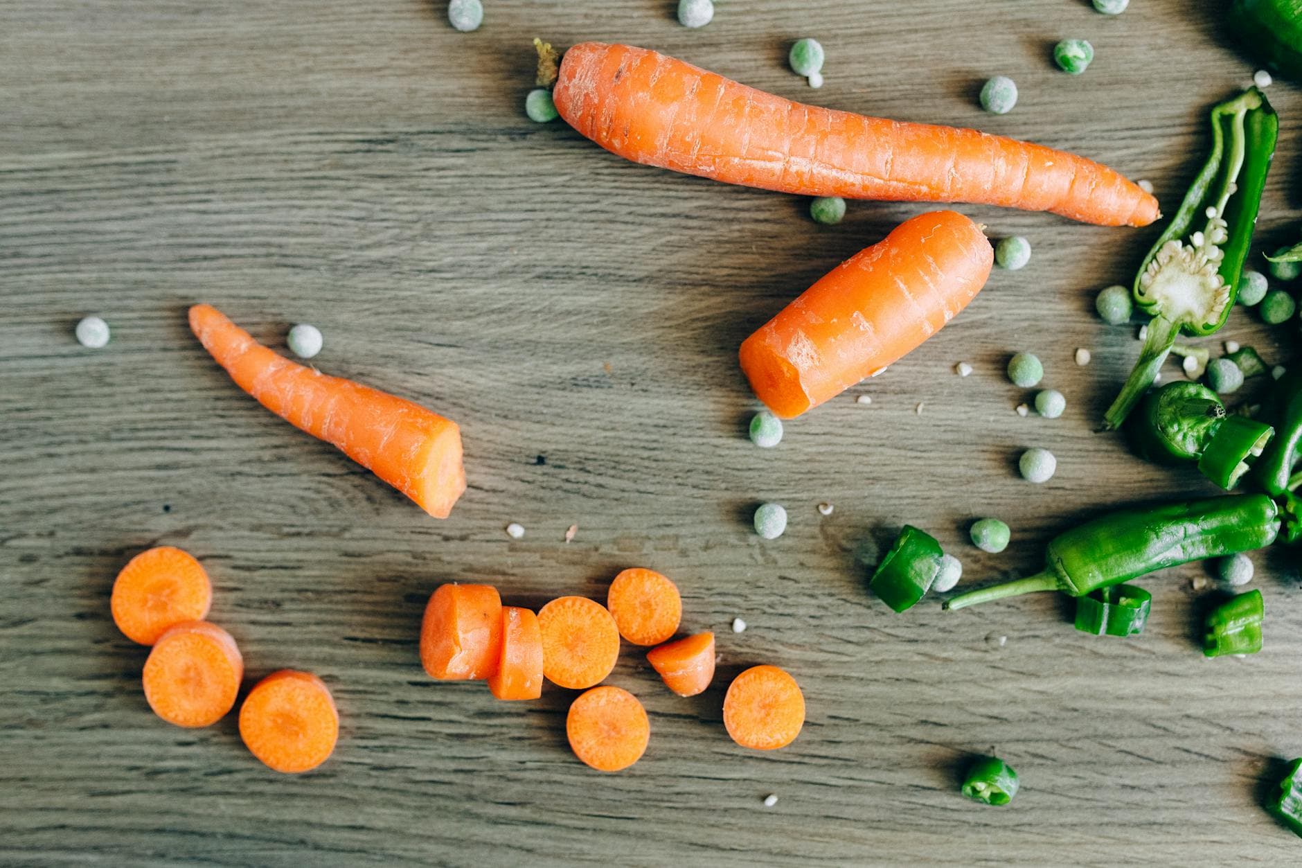 Flat lay of fresh carrots, peas, and green chilies on a rustic wooden surface. - spring produce recipes