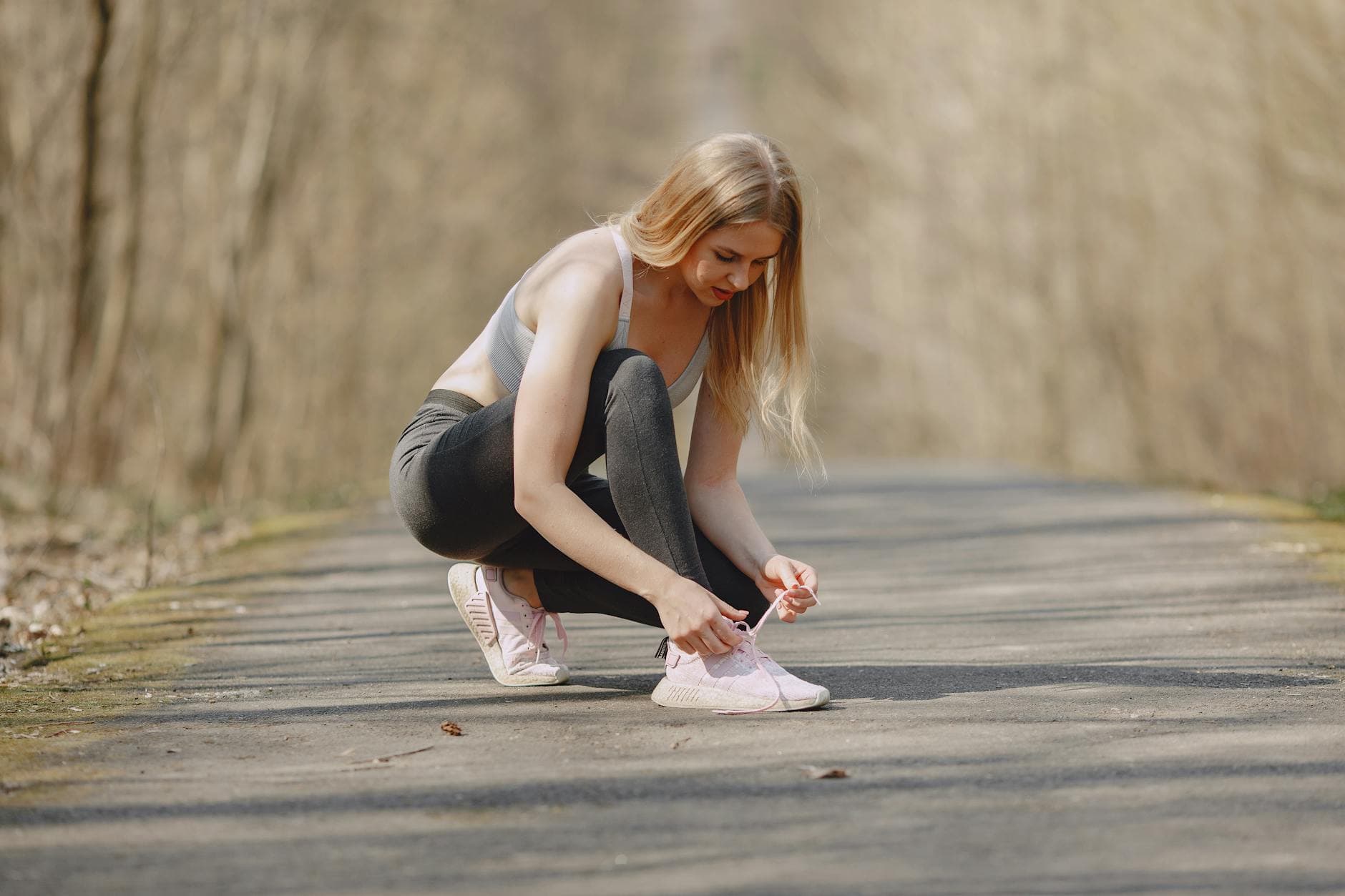 Full body young female jogger in sportswear sitting on path in spring park and tying shoelaces on sneaker while resting after training outside - spring run nutrition