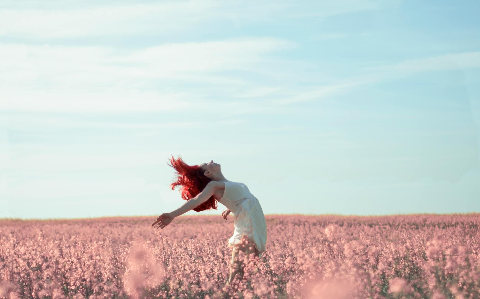 Woman with red hair in a white dress expressing freedom in a vibrant summer field. - spring sad triggers
