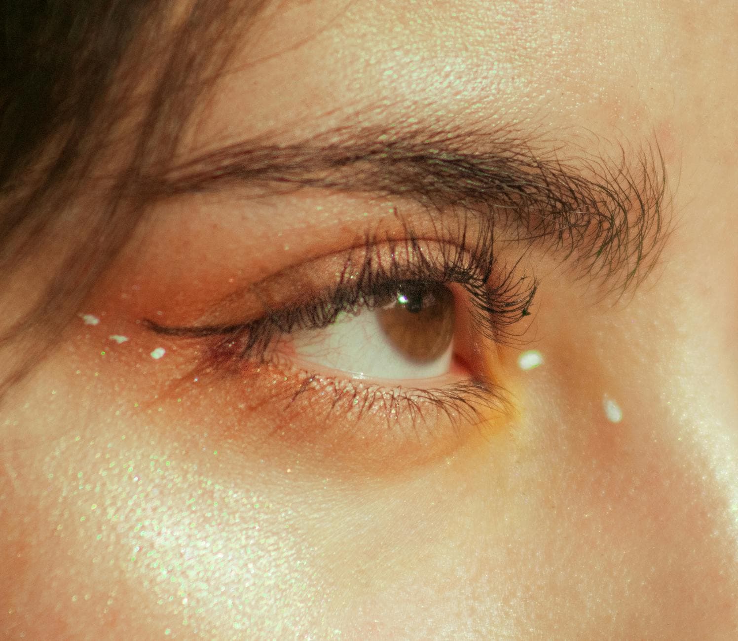 Detailed close-up of a woman's eye with shimmering makeup and artistic accents. - spring skin glow