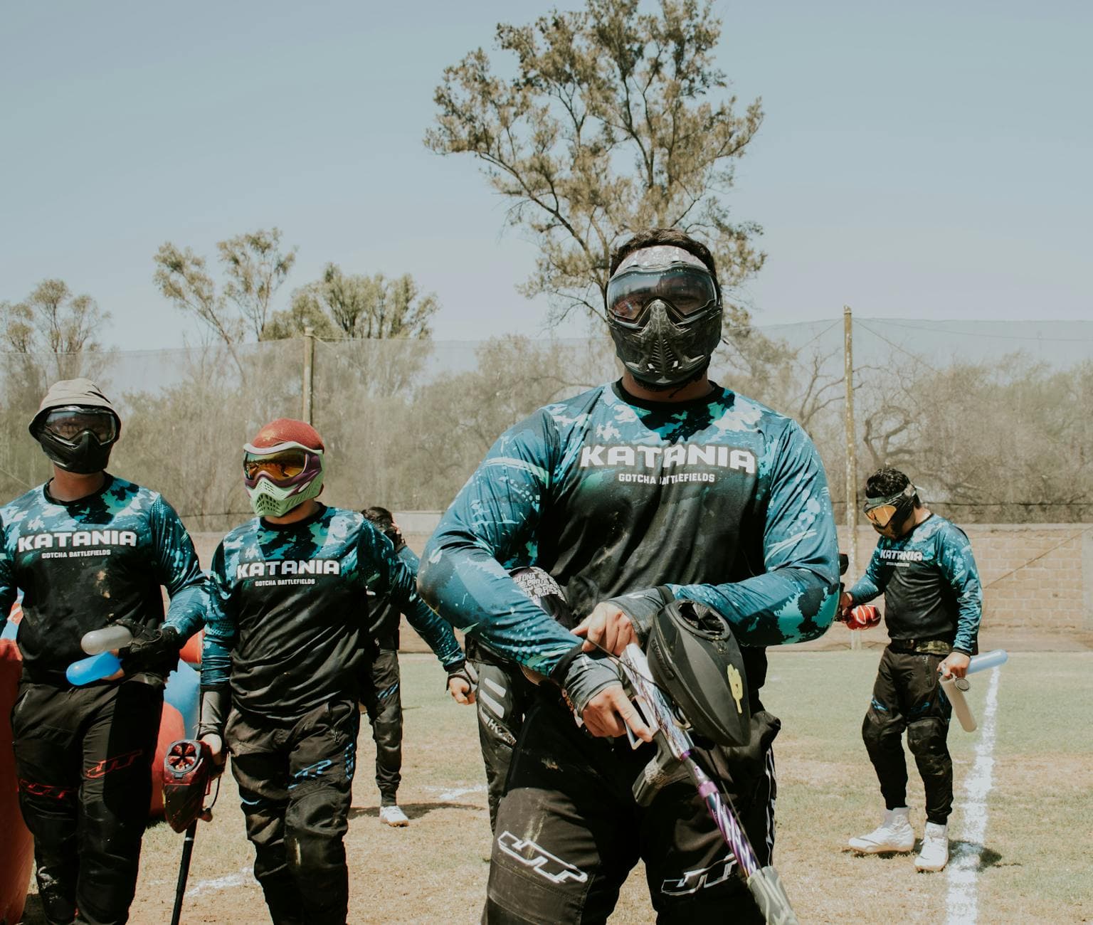 Group of men playing paintball outdoors, wearing protective masks and gear. - spring training gear