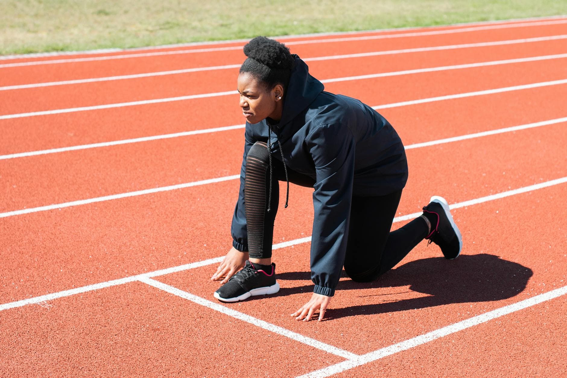 Female athlete in starting position on a sunny day at the track. - strength training runners