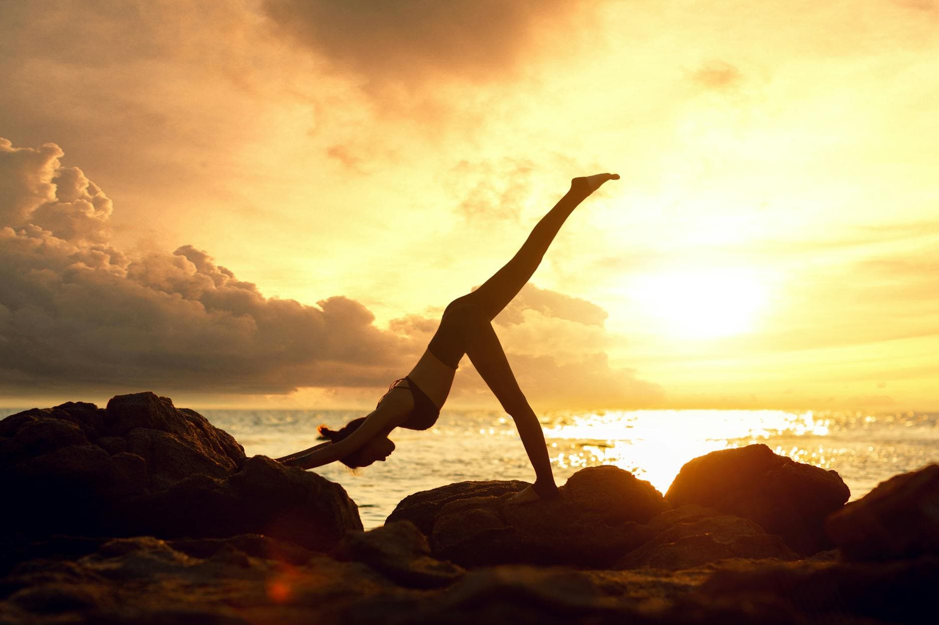 Silhouette of a woman practicing yoga on rocks by the sea during a stunning sunset. - sunrise yoga spring