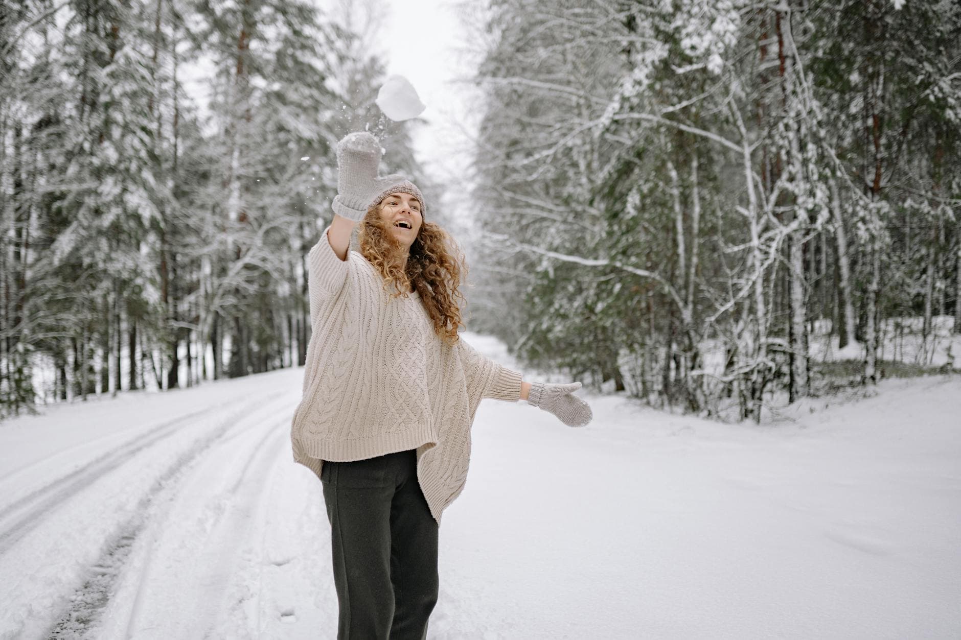 Woman throws a snowball in a snowy forest, expressing joy and playfulness in a winter landscape. - winter body reset