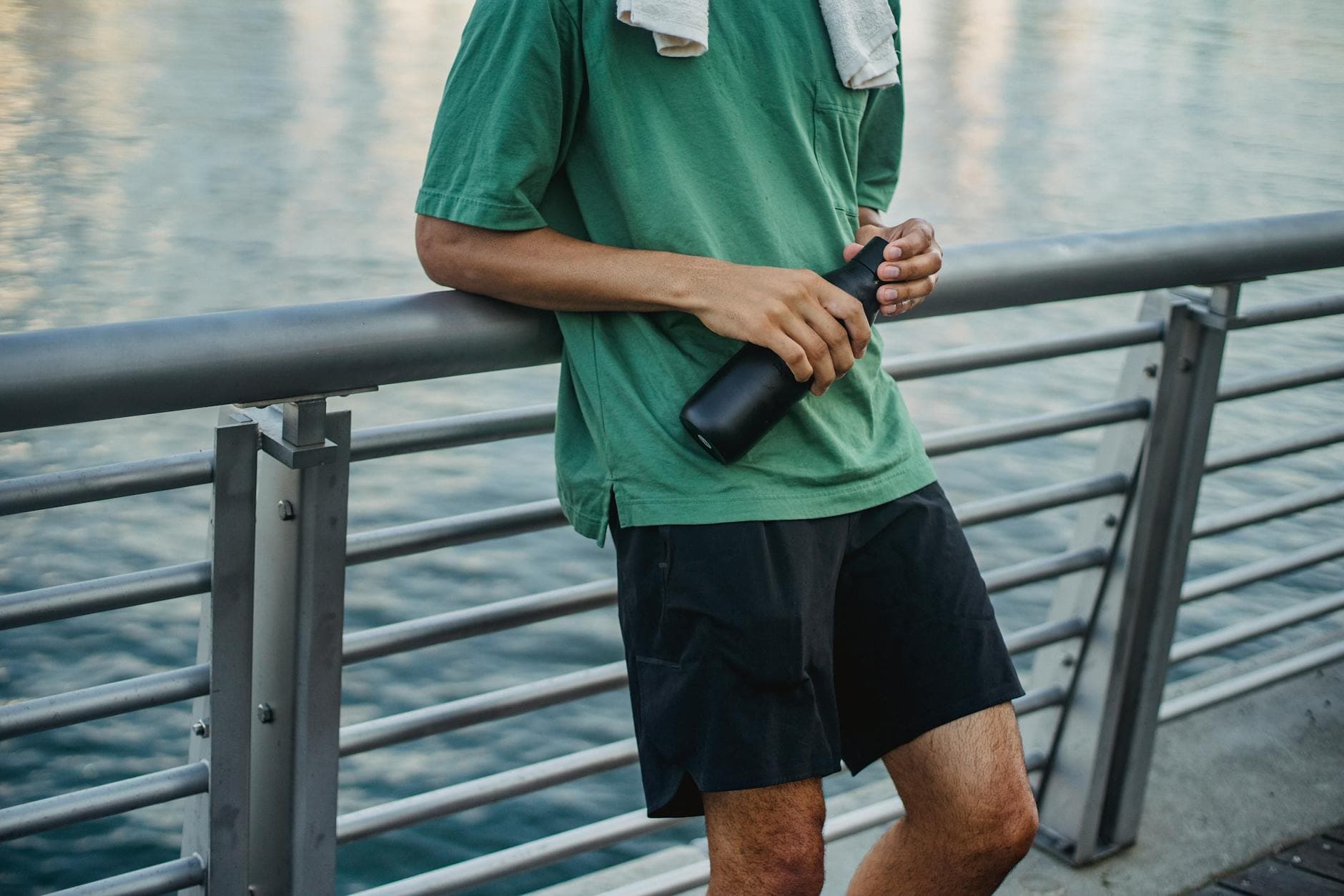 Male in activewear leaning on a railing holding a water jug by the water, post-exercise. - 4 day workout routine