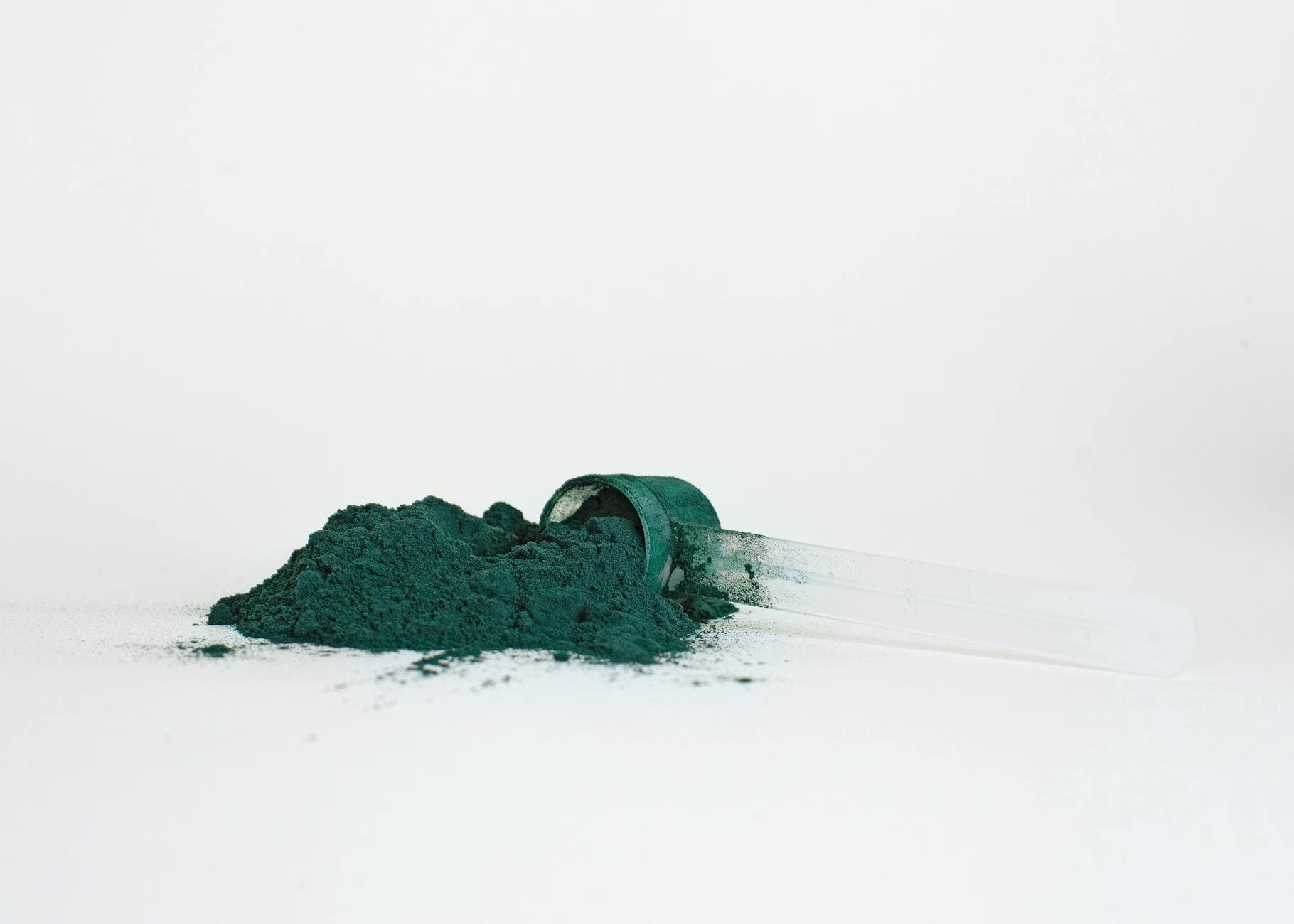 A pile of spirulina powder in a transparent measuring scoop isolated on a white background. - best plant based protein powder
