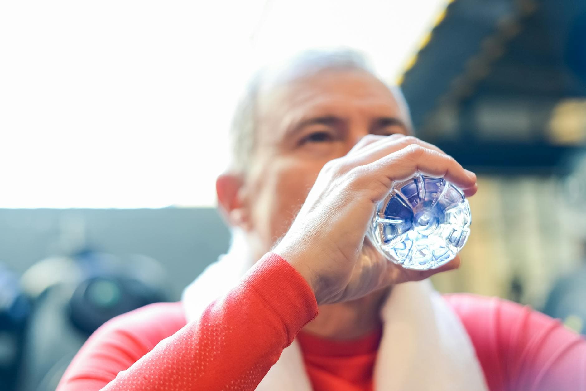 Elderly man in red shirt sipping water during gym session. - best post workout drink