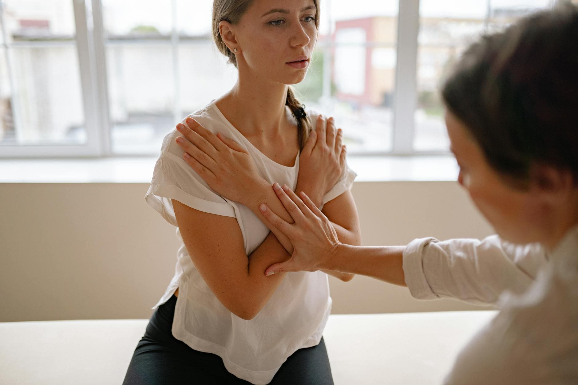 Therapist guiding a woman in a stretching exercise indoors, focusing on physical therapy. - correct shoulder posture exercises