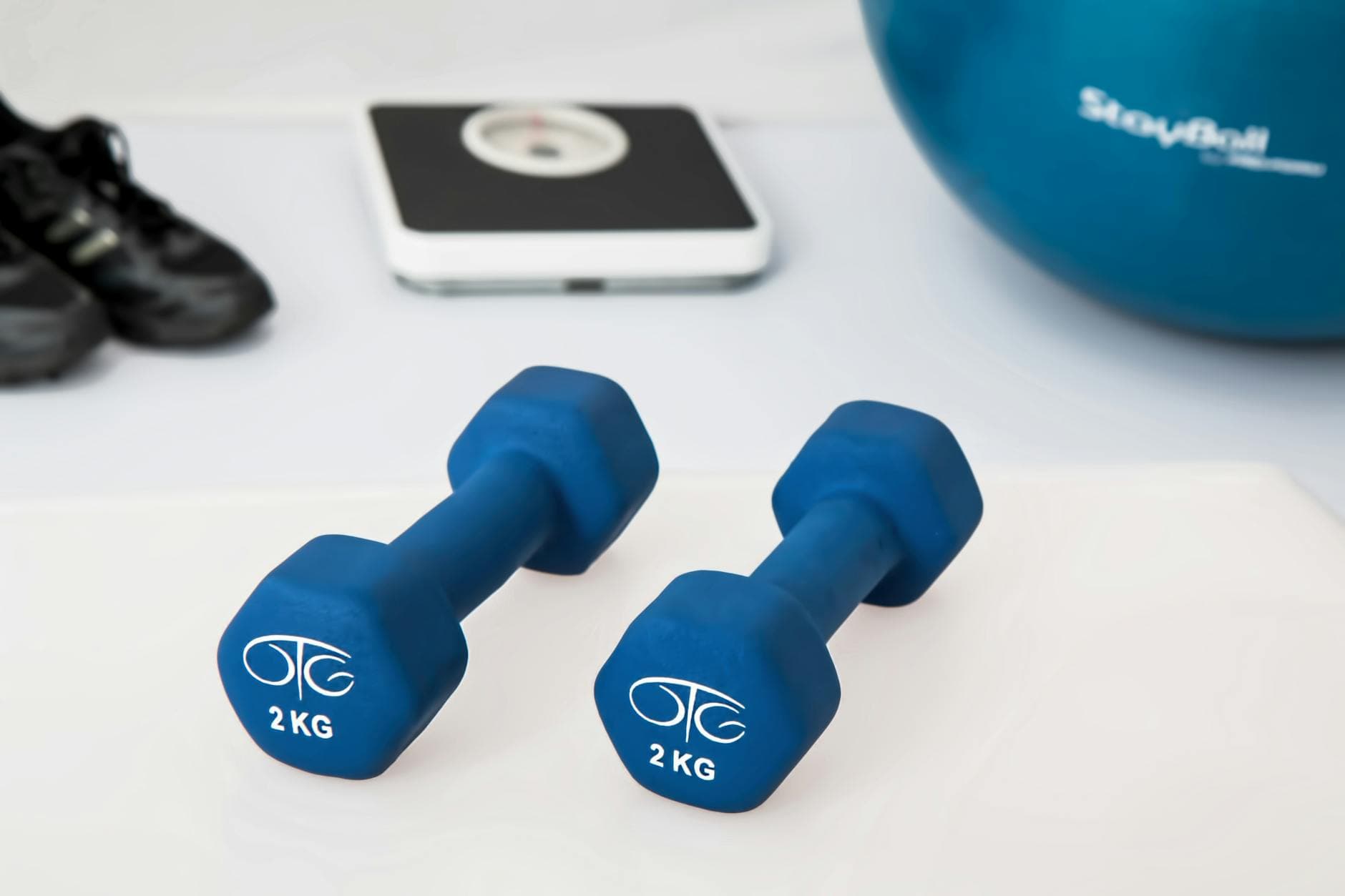 Blue dumbbells placed on a white surface with fitness equipment in the background. - no equipment home workout