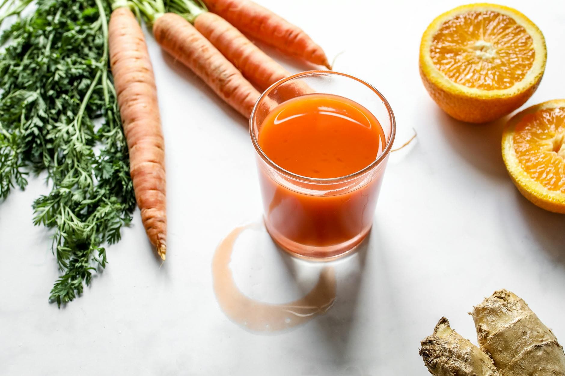 A refreshing glass of carrot, orange, and ginger juice surrounded by fresh ingredients on a white background. - immune boosting foods list