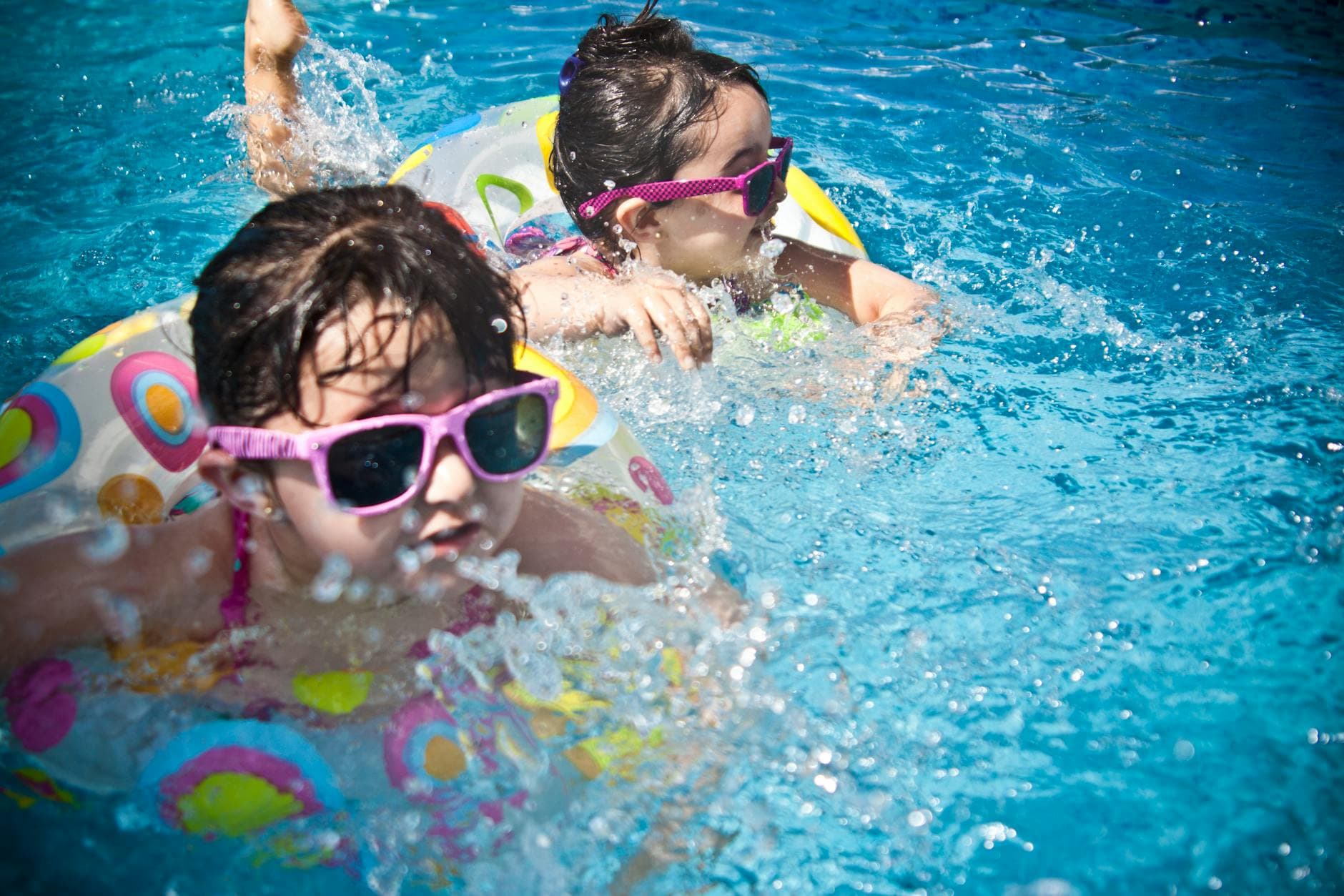 Two young girls enjoying a playful day in a bright blue swimming pool with colorful float rings. - swimming benefits for children