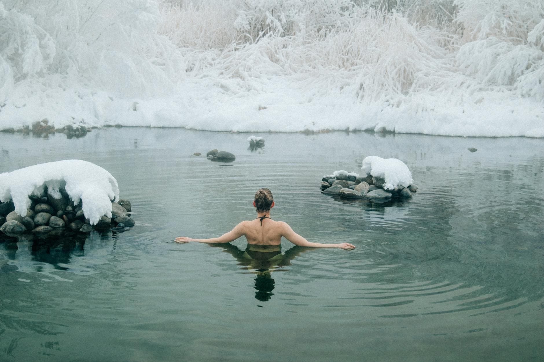 A young woman enjoying a swim in a tranquil winter lake surrounded by snow. - swimming benefits women