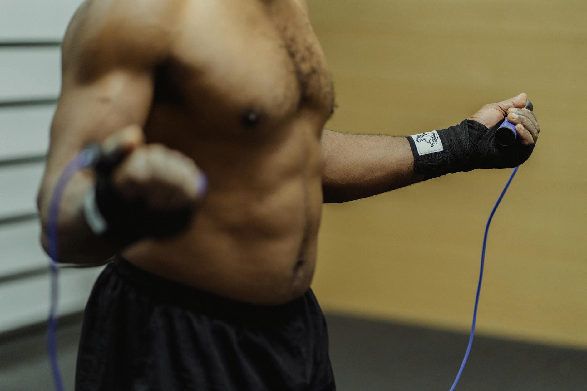Focused shirtless man exercising with a jump rope indoors, emphasizing fitness and discipline. - upper body cardio workout