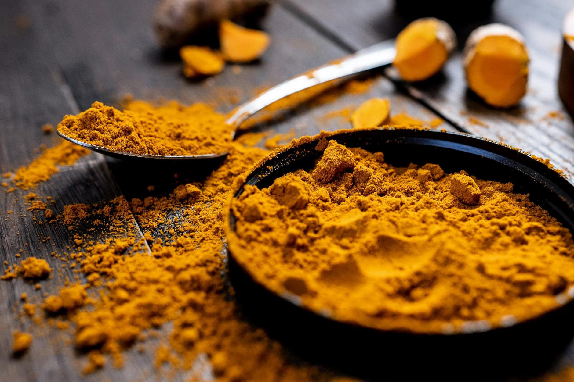 Close-up of vibrant turmeric powder with root on rustic wooden table, emphasizing texture and color. - best anti inflammatory foods