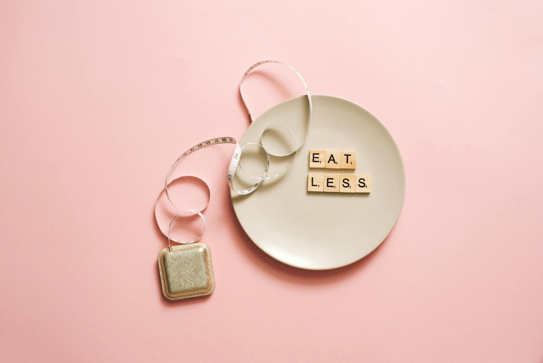A motivational image featuring a plate with scrabble tiles spelling 'Eat Less' on a pink background. - best diet plan