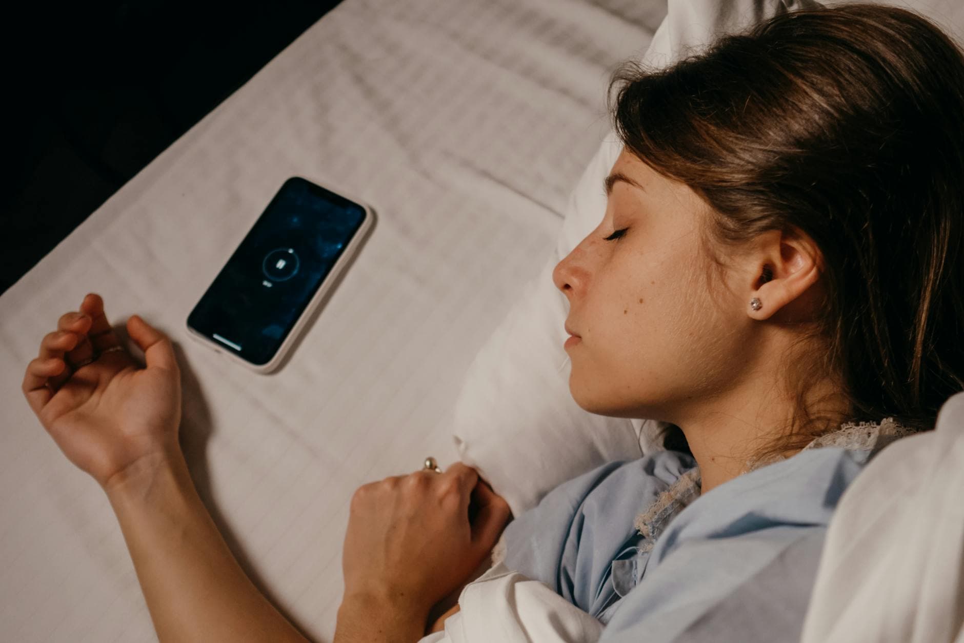 A woman sleeping peacefully in bed beside her smartphone, capturing a serene bedtime moment. - daylight sleep science