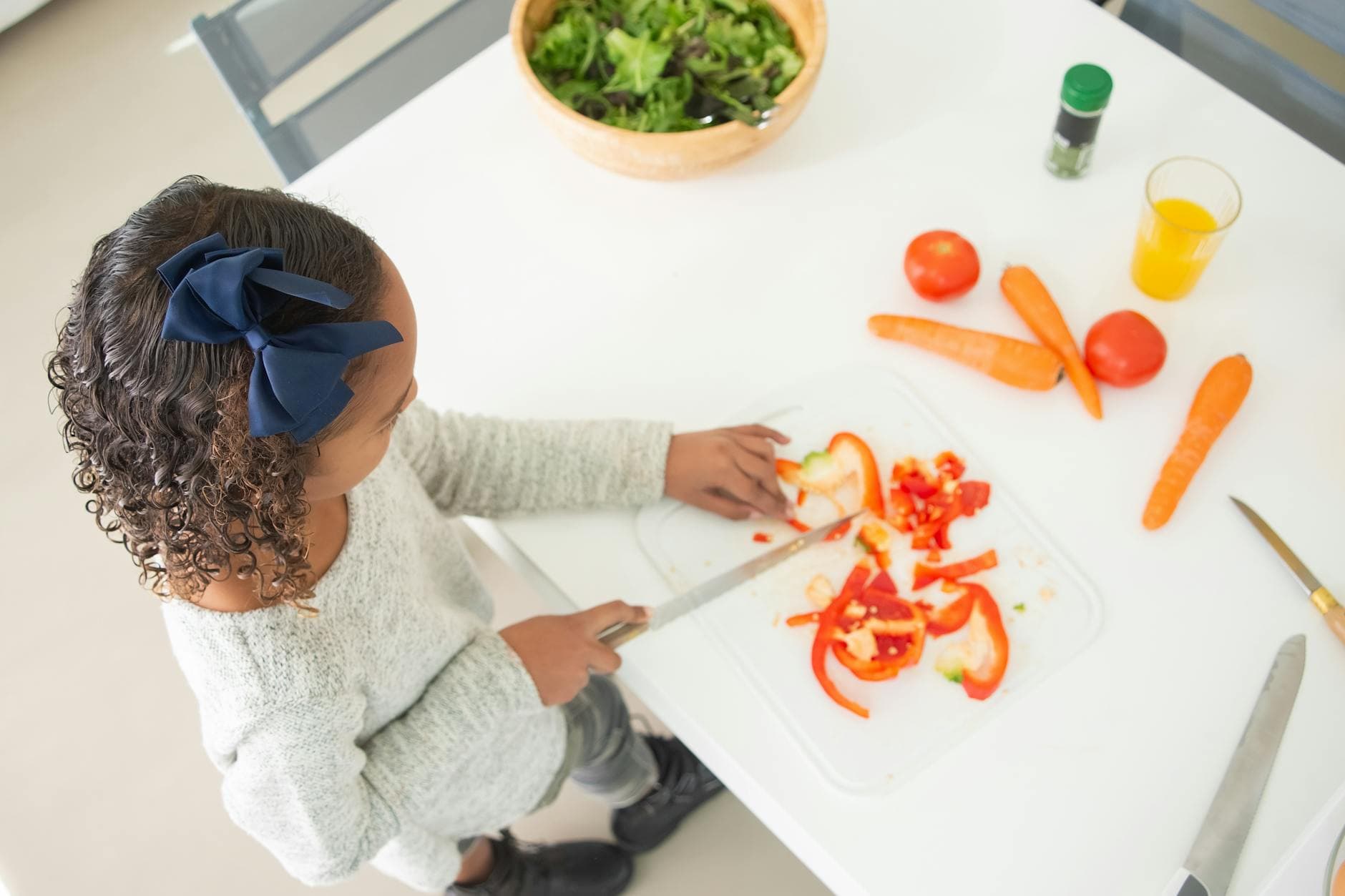 A child slicing peppers for a fresh salad in a bright kitchen setting. - healthy kid meals