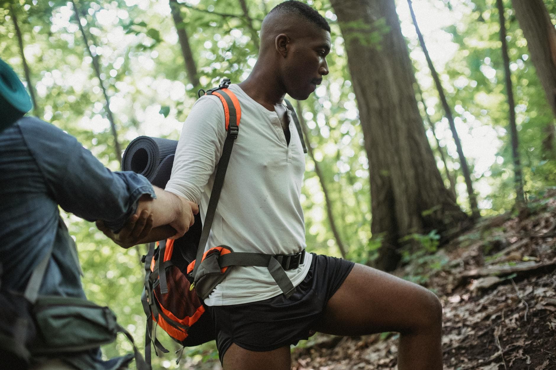 Hiker climbing through a forest trail with a friend's support. Perfect for adventure and teamwork themes. - hiking calorie burn