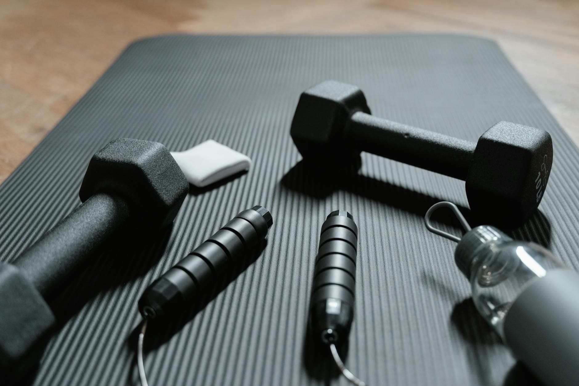 Close-up of dumbbells, jump rope, and water bottle on a yoga mat, ideal for home fitness routines. - home cardio workout
