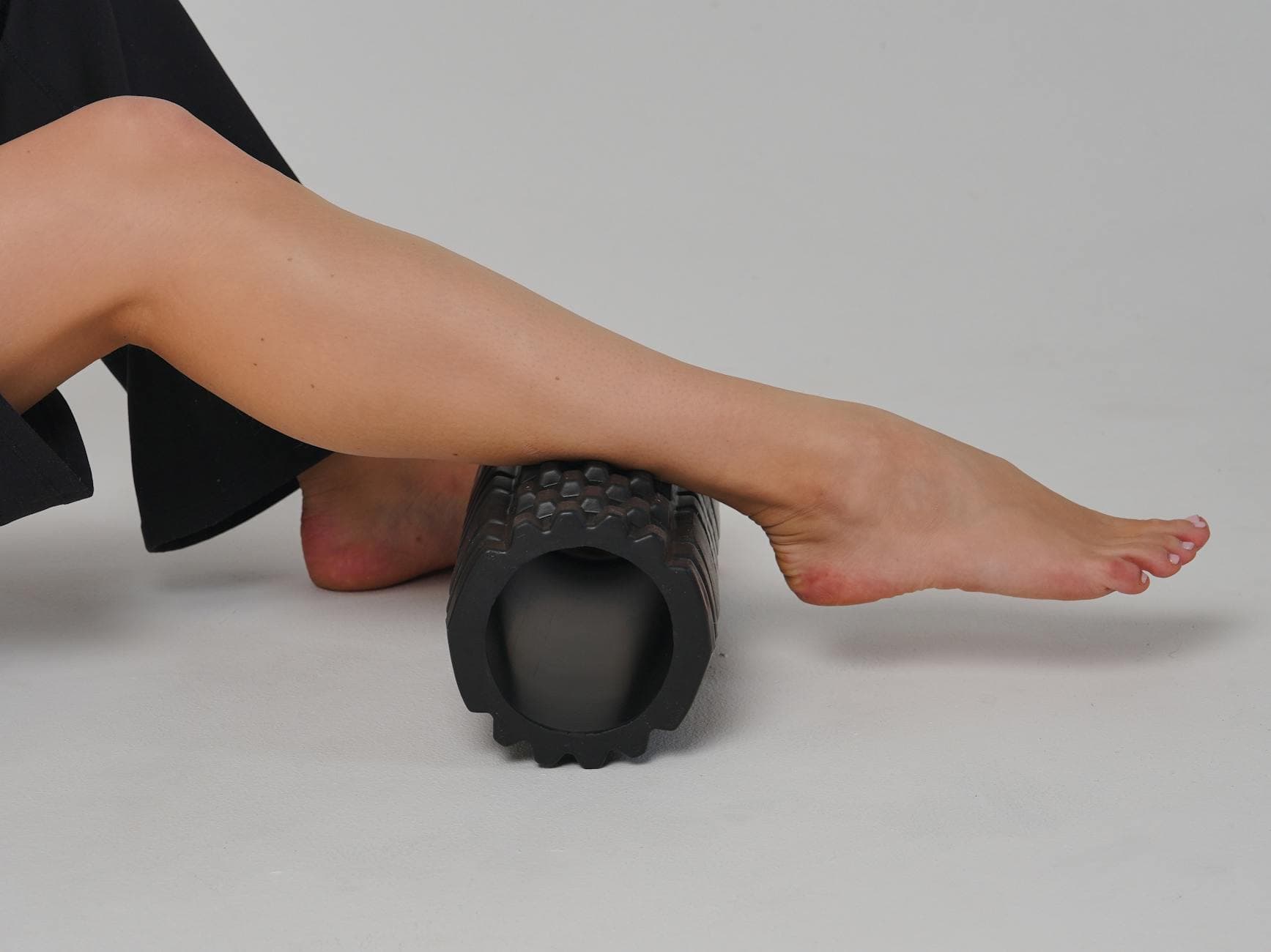 Close-up of a leg using a foam roller for stretching and muscle relief in a studio setting. - lower back flexibility exercises