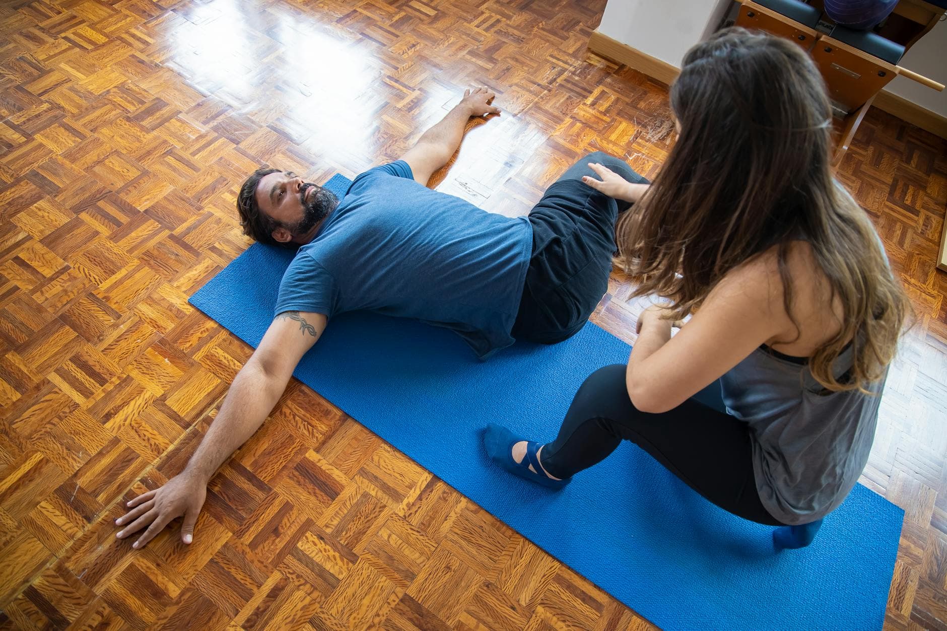 A man and woman engaged in a rehabilitation exercise on a yoga mat indoors. - pilates ring exercises