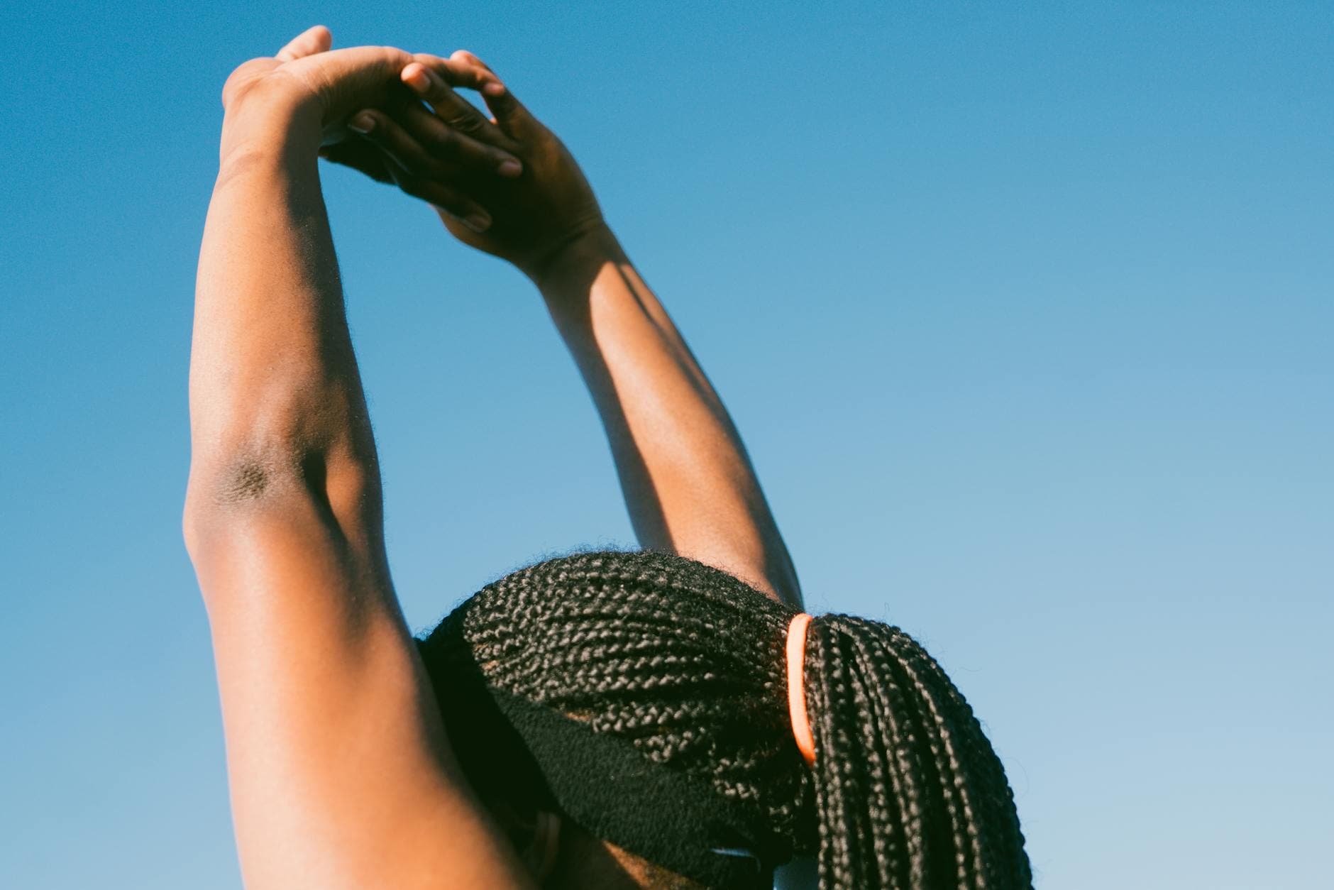 Person stretching outdoors with braided hair against a clear blue sky for a healthy lifestyle concept. - stretching routine men