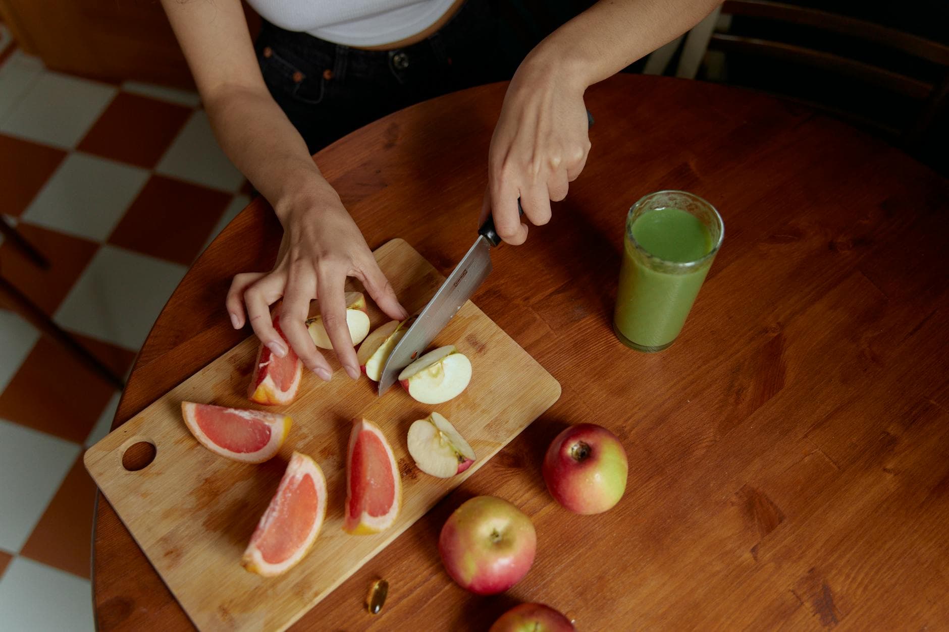 A person slicing apples and grapefruit on a cutting board next to a glass of green juice. - weight loss smoothies