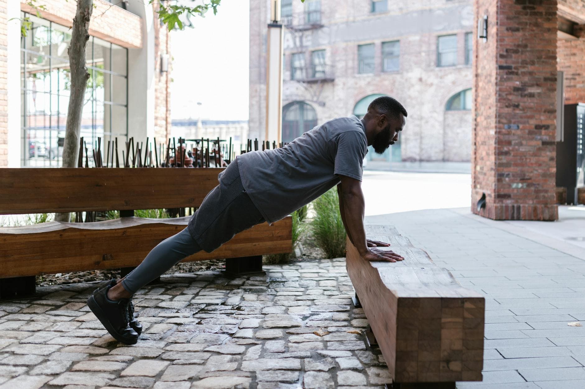 African American man performing push-ups outdoors in an urban setting, showcasing strength and fitness. - core workout day