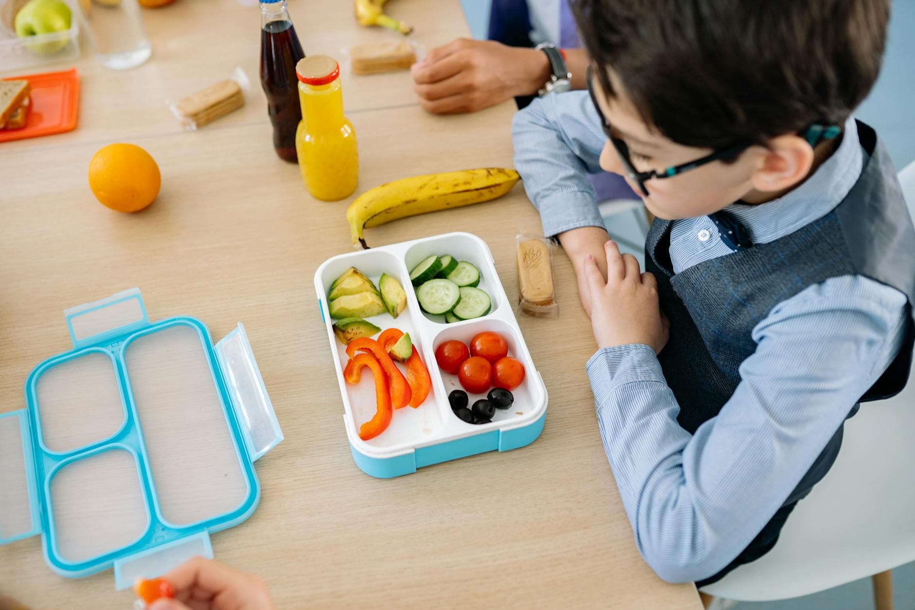 A young boy sits at a wooden table in school, enjoying a healthy lunch from a colorful lunchbox. - easy healthy lunches