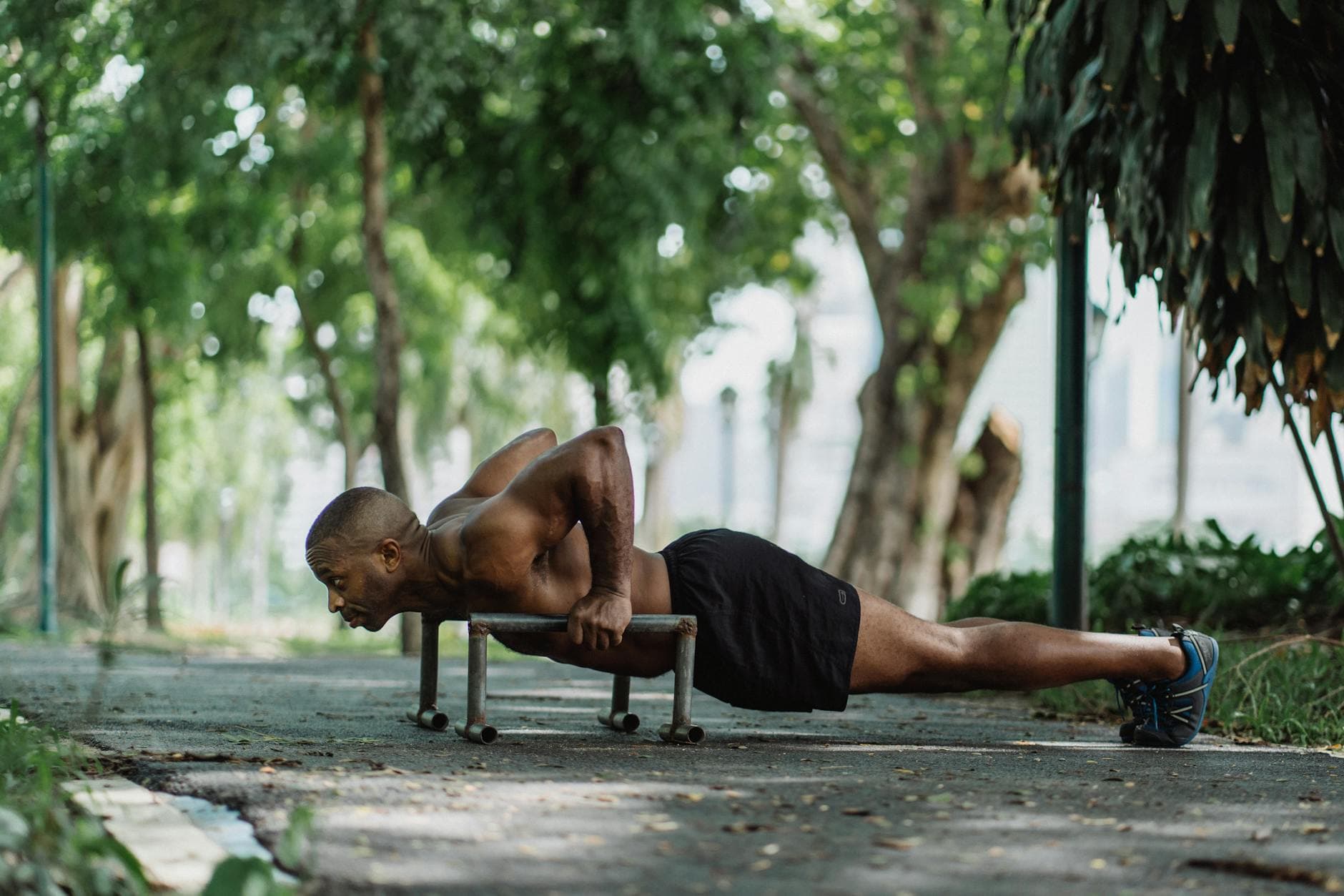 Fit man doing push-ups on low dip bars outdoors in a green park. - gardening strength training