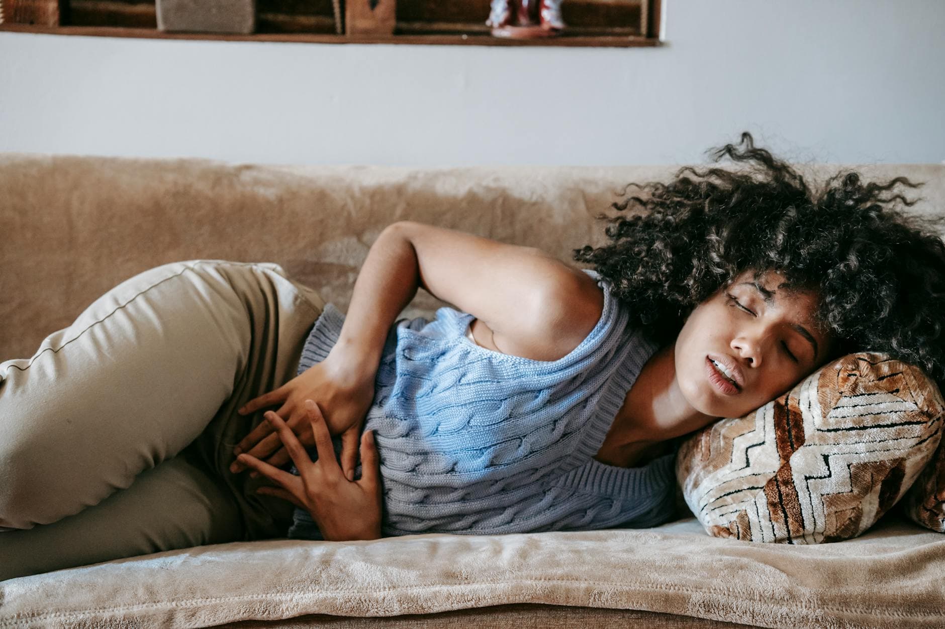 Young African American female with closed eyes lying on sofa while having acute stomach ache - gut health reset