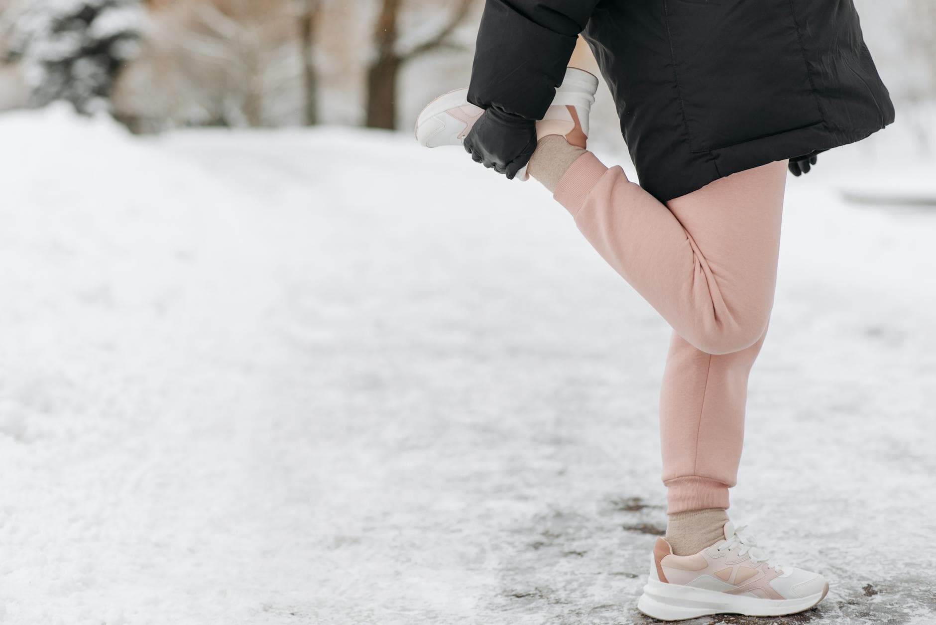 Person stretching in the snow, wearing winter attire and sneakers, in a serene outdoor setting. - post winter workouts