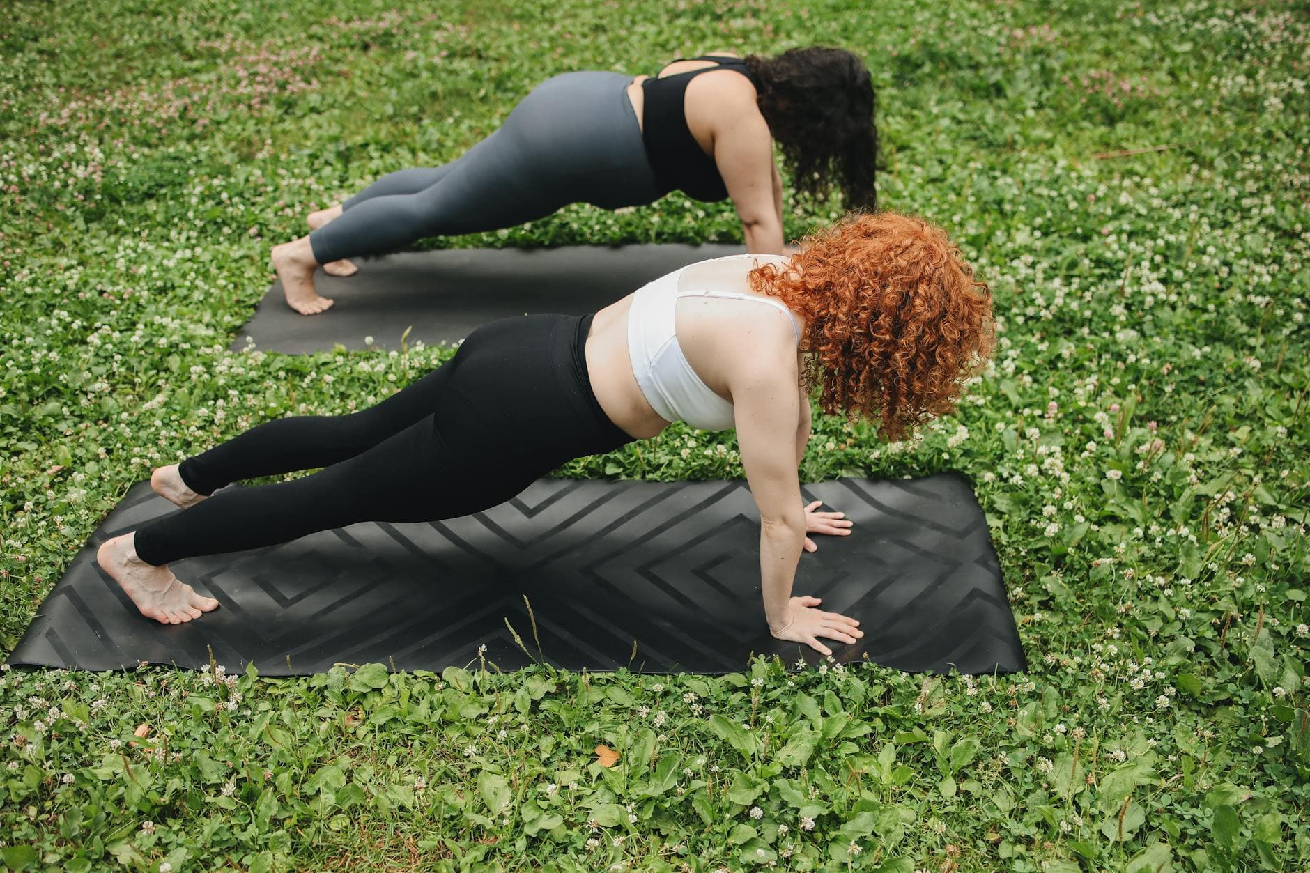 Two women holding a plank position on yoga mats outdoors in a lush green setting. - spring outdoor workouts