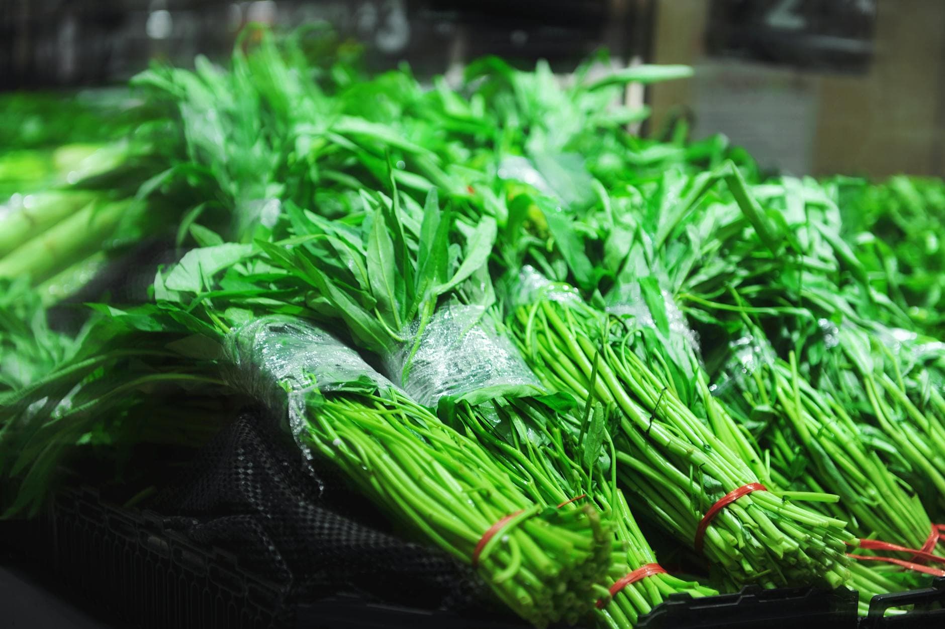 Close-up of fresh green vegetables neatly bundled with red ties at a market. - spring produce health