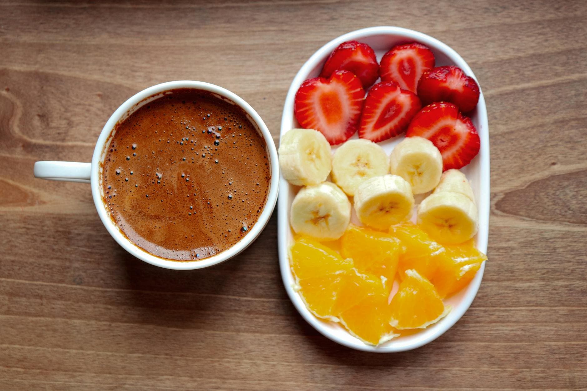 Top view of a nutritious breakfast featuring a coffee and a plate of fresh fruits: strawberries, bananas, and oranges. - energy boosting foods