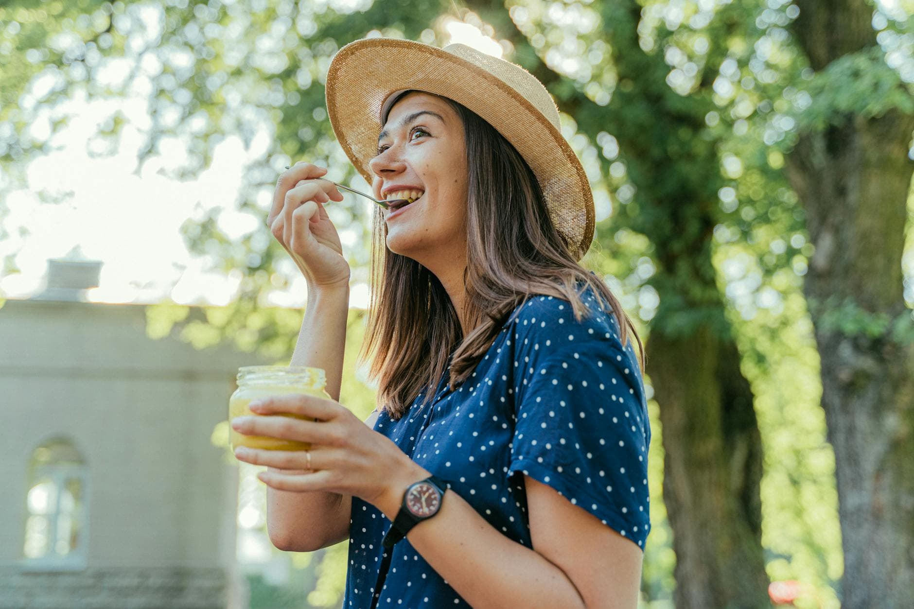 Smiling woman wearing a hat enjoys a dessert outdoors under sunlight. - gut health allergies