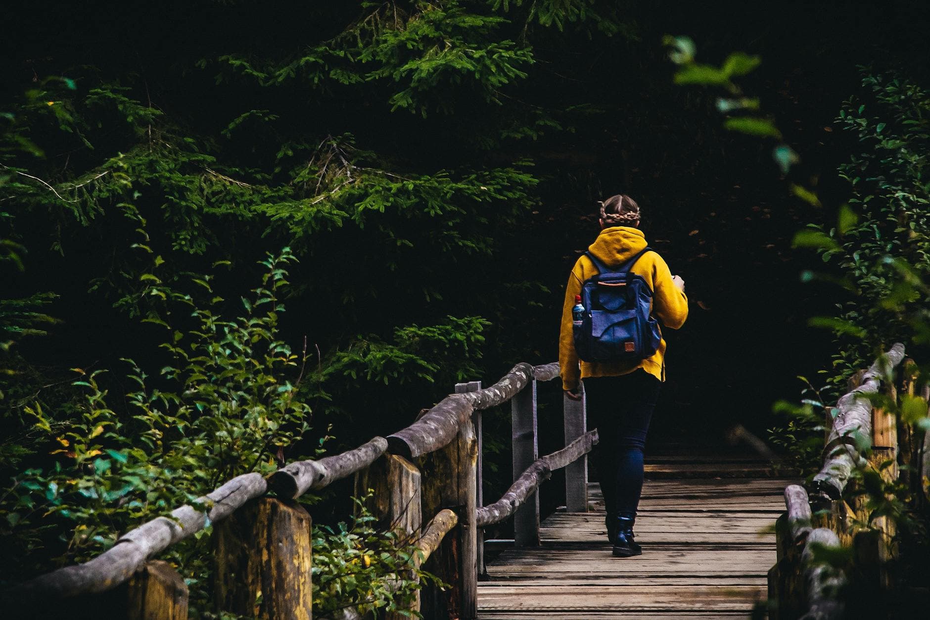 Person with backpack crossing wooden bridge in a forest, embracing nature. - mindful walking nature