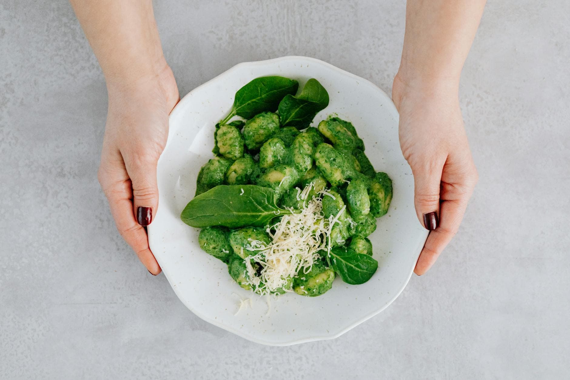 Top view of spinach gnocchi garnished with cheese on a plate, held by hands. - spring healthy recipes