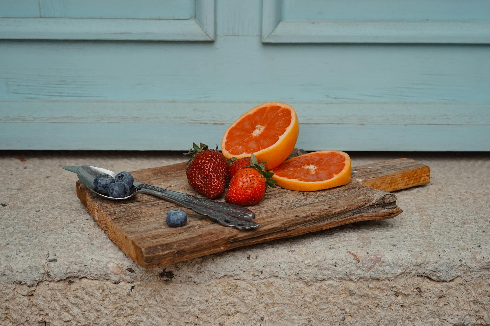 A rustic display of strawberries, oranges, and blueberries on a wooden board against a blue backdrop. - spring nutrition outdoor