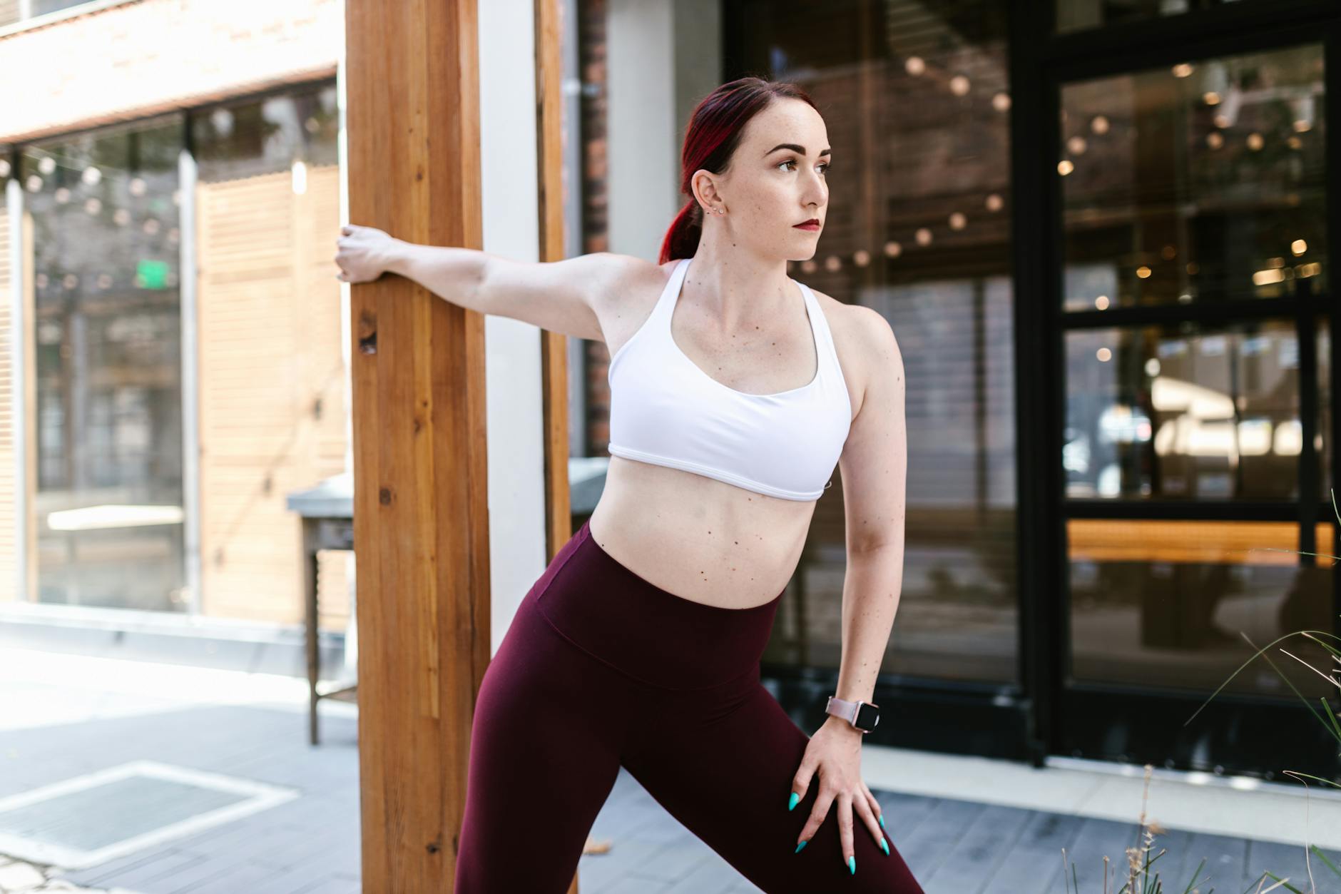 A woman in sportswear stretching by a wooden pillar in an urban outdoor setting. - 4 day workout routine