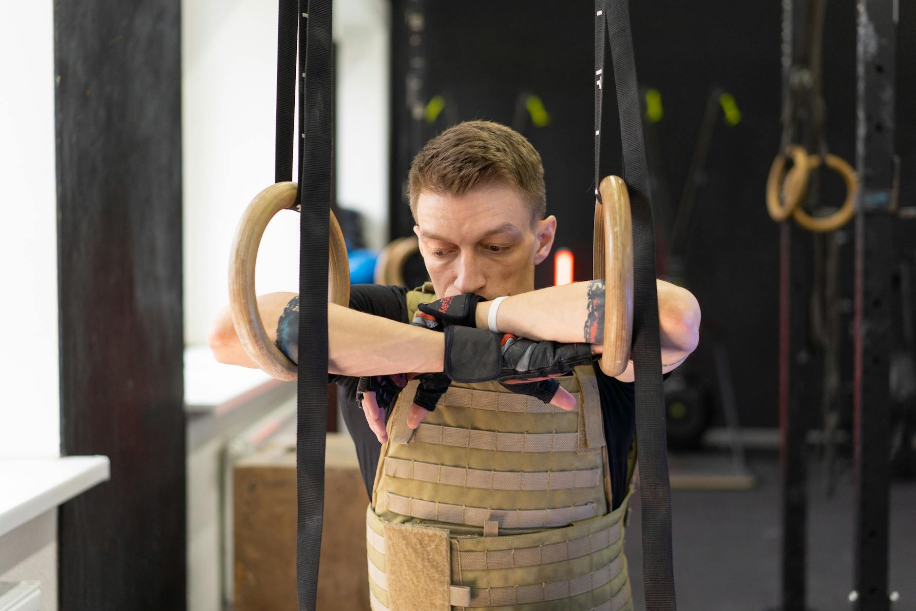 A serious athlete in a weighted vest takes a focused break on gymnastic rings in the gym. - best core workout routine
