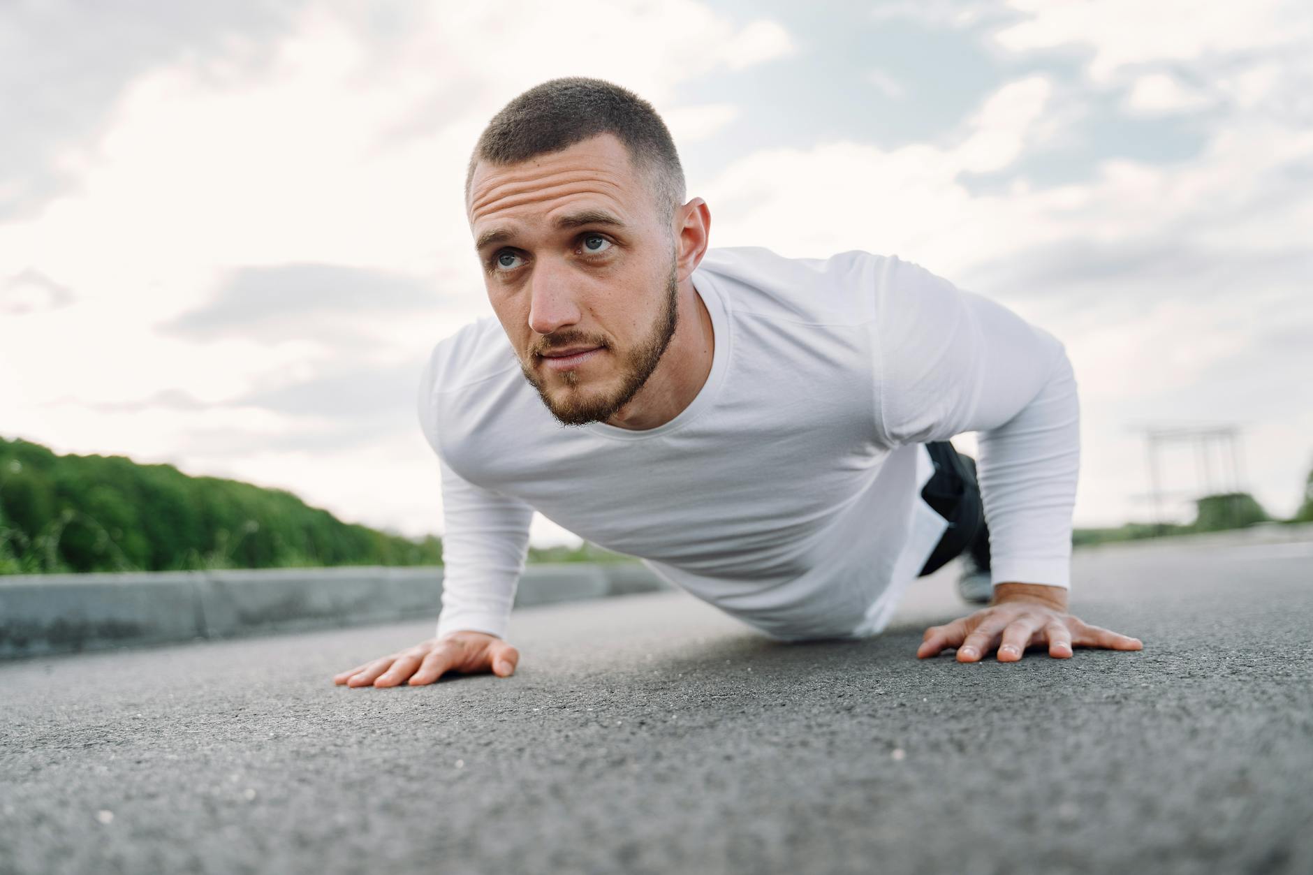 Focused man in sportswear doing push-ups on a road in a natural setting. - best core workout routine
