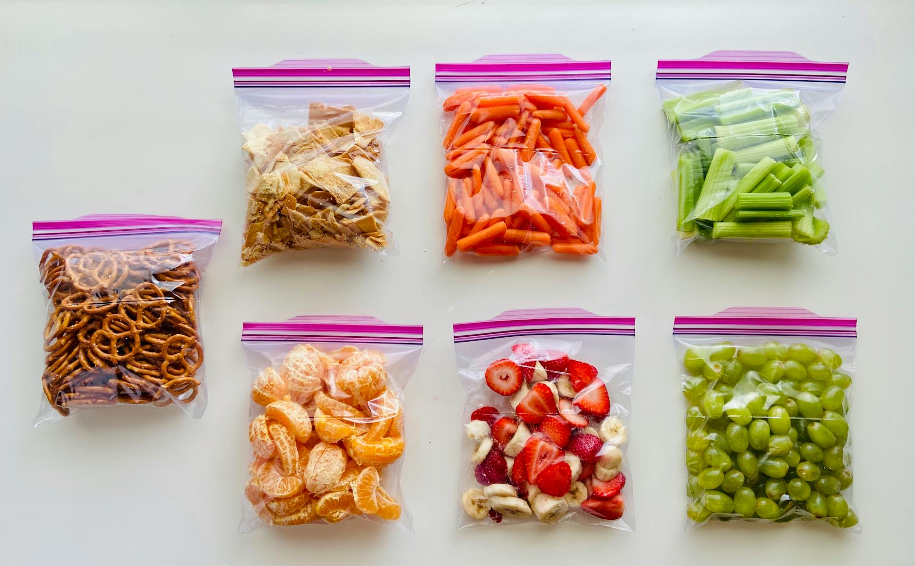 An assortment of fruits, vegetables, and snacks neatly packed in zip lock bags on a white background. - best costco healthy snacks