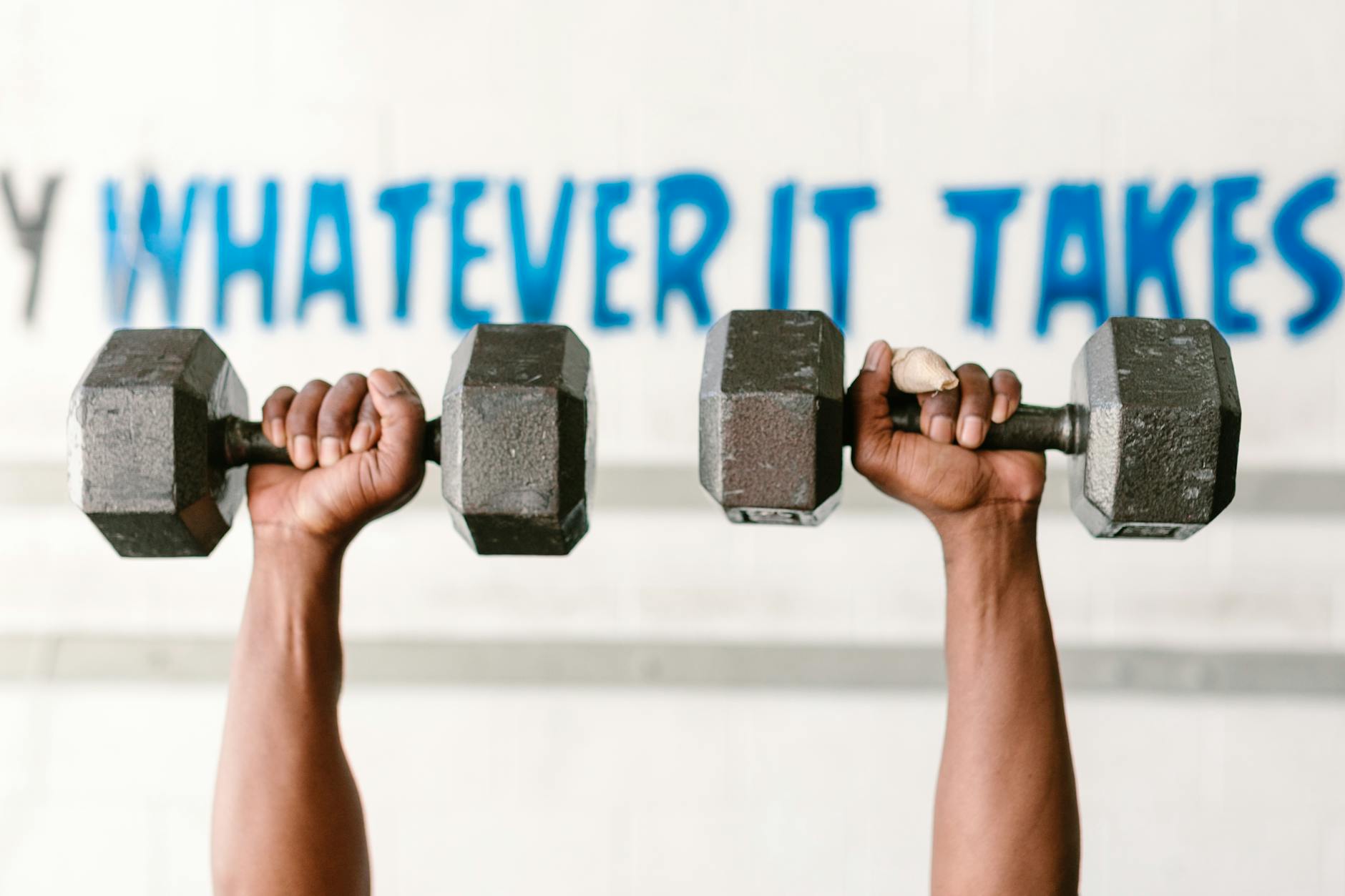 Hands holding dumbbells against motivational text "Whatever It Takes" in a gym setting. - best at home cardio