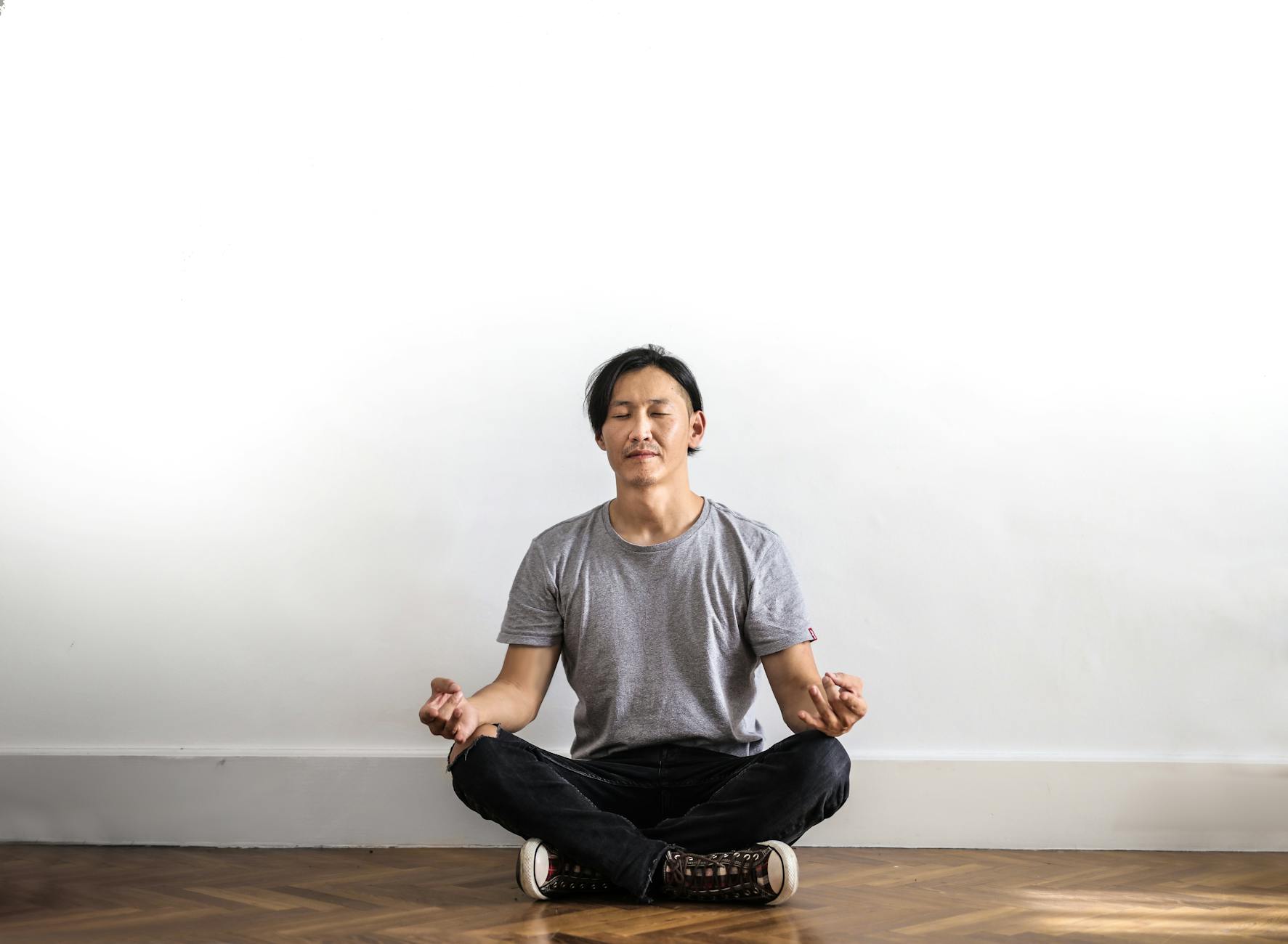 Asian man practicing meditation indoors on a wooden floor, promoting relaxation and mindfulness. - best mindfulness meditation techniques