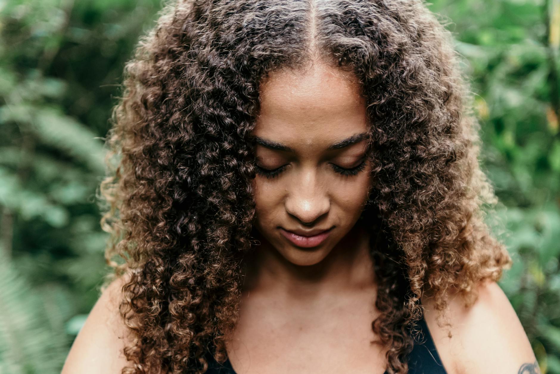 A serene woman with curly hair meditates peacefully in a lush outdoor setting. - best mindfulness meditation techniques