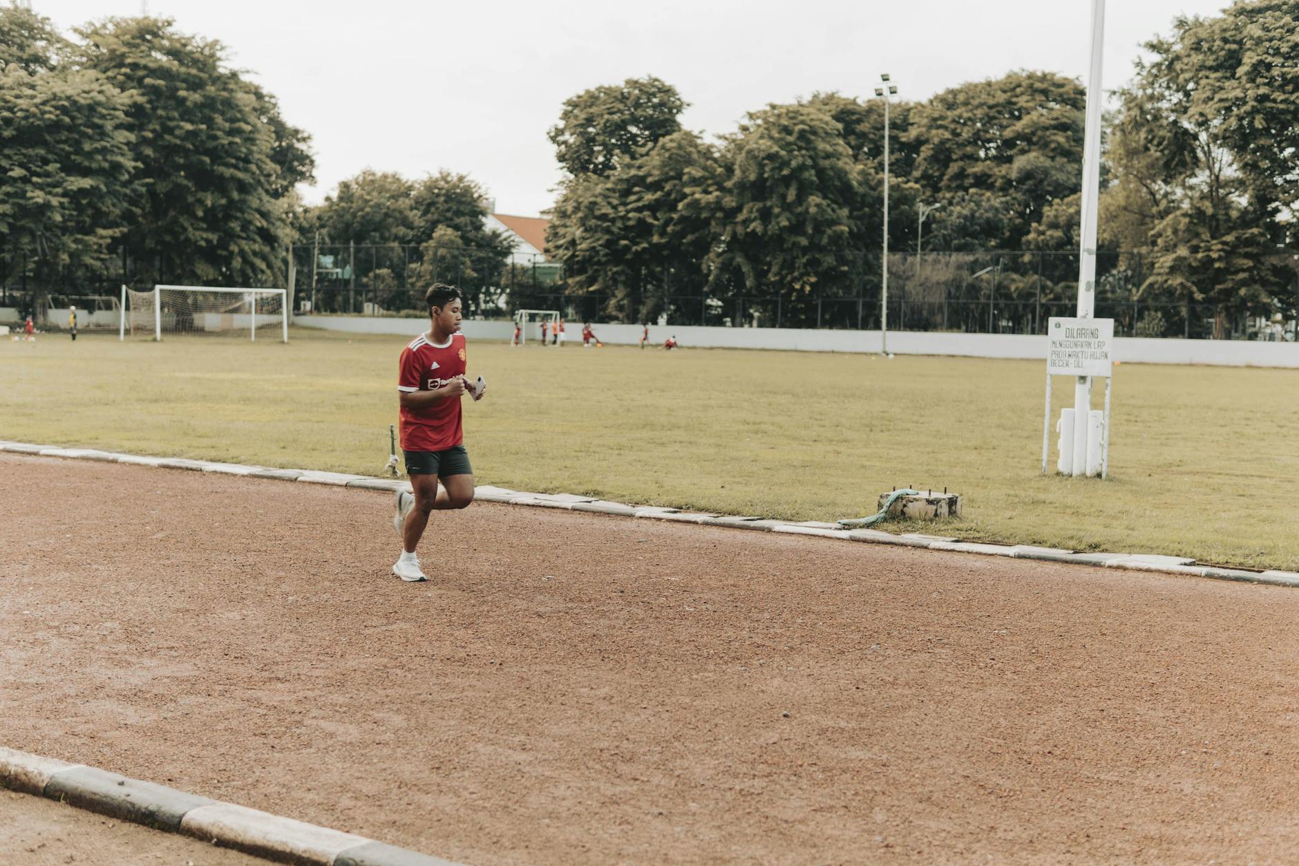 A young man in athletic attire jogging on an outdoor track in a park setting. - best morning exercises