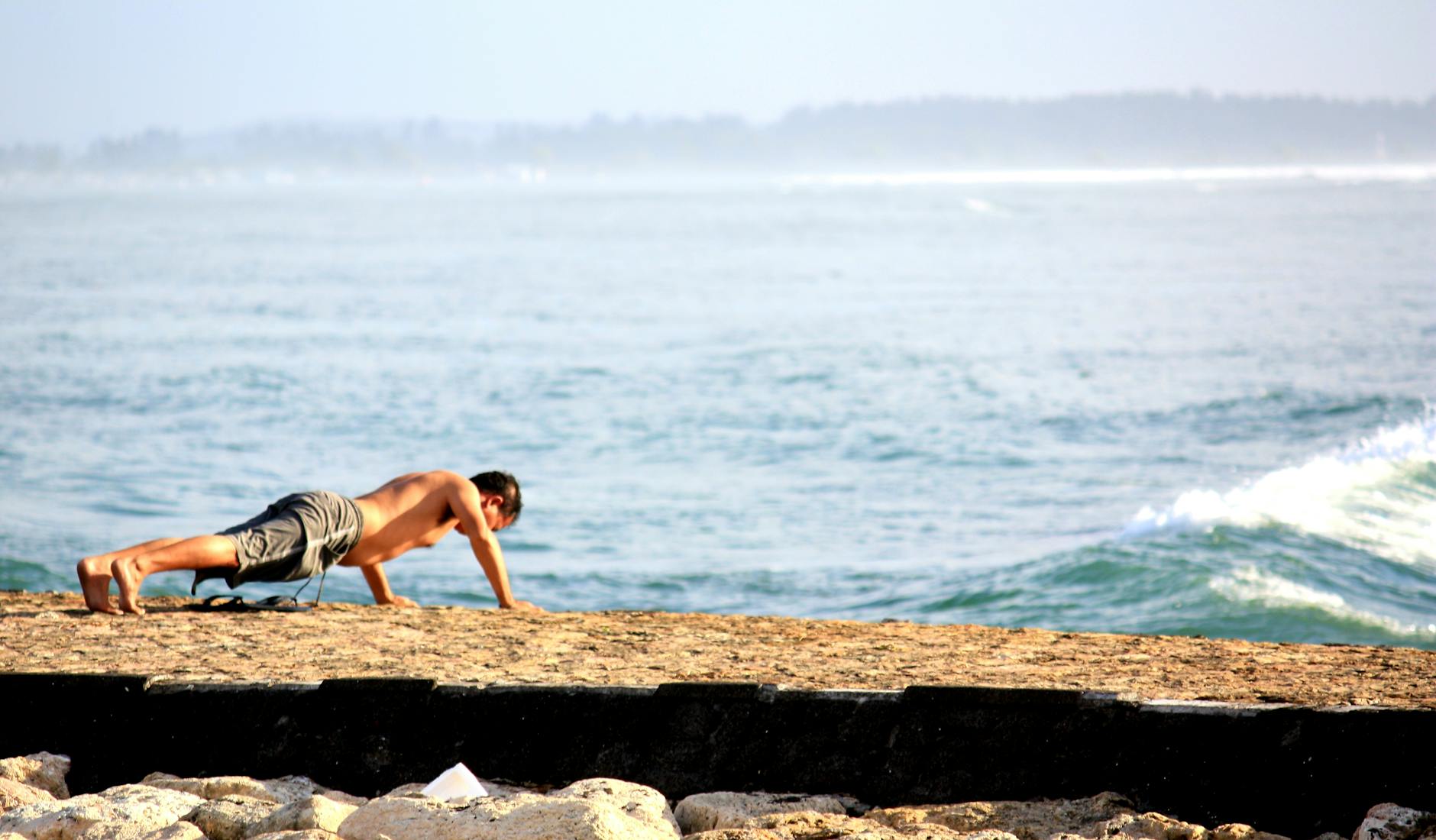 Fit man exercises with push-ups by the ocean on a sunny beach day. - bodyweight exercises for beginners
