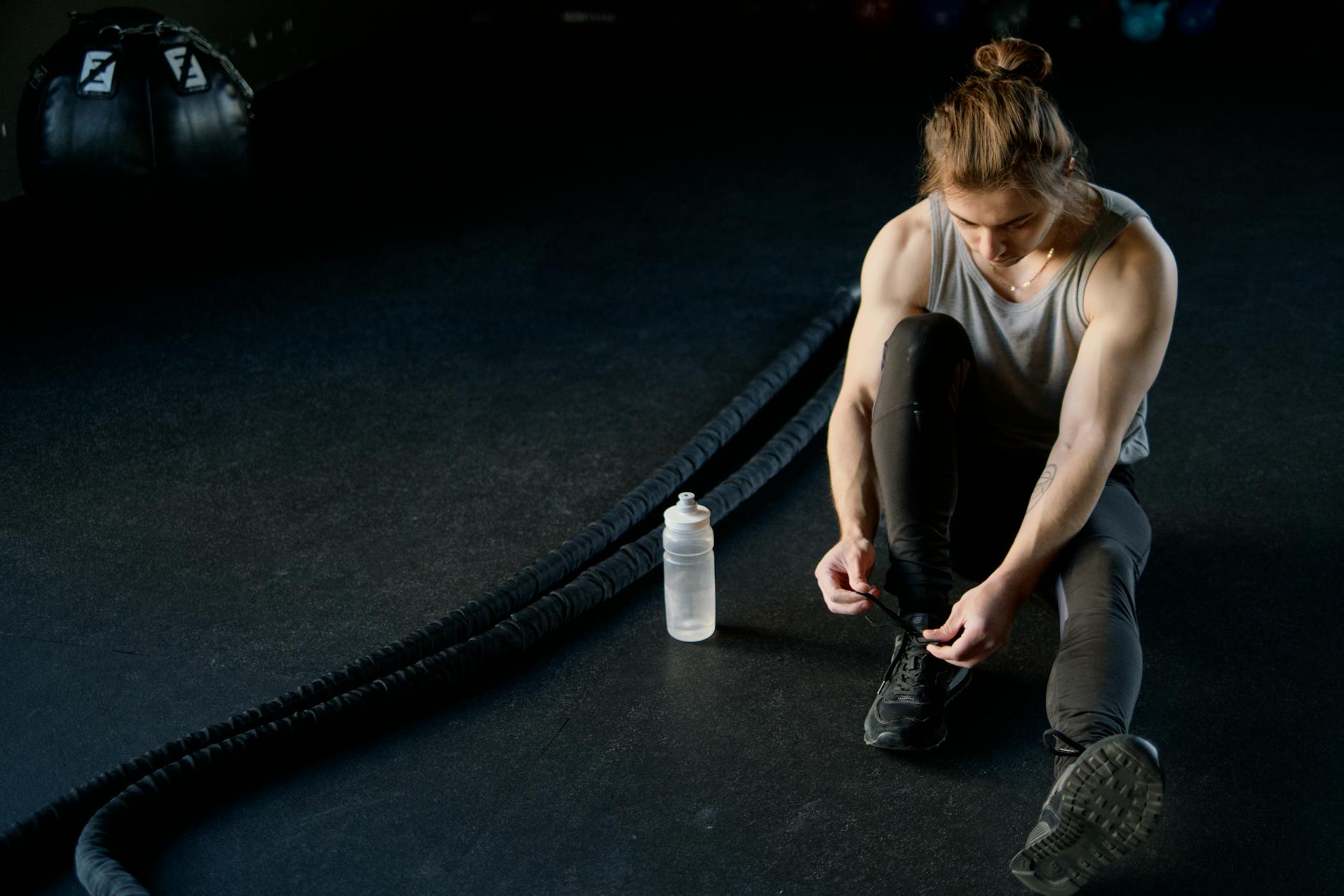 Man tying shoes on gym floor with battle ropes and water bottle, ready for training. - c4 pre workout ingredients