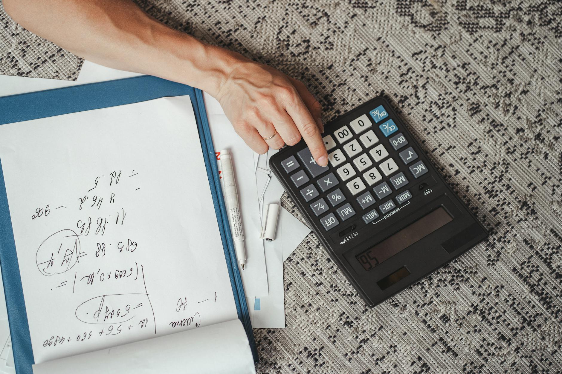 Top view of a hand calculating numbers with a large calculator and notes on a desk. - calorie deficit calculator
